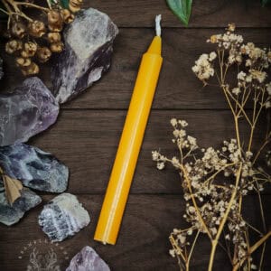 A single orange chime candle on dark wood, with raw amethyst to the left and dried baby's breath to the right.