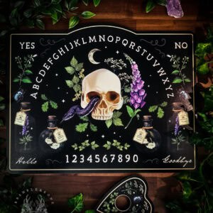 A Poisonous Plants spirit board displayed on dark wooden decking, surrounded by lush green foliage. The black board features a central skull with purple snake emerging from it, flanked by poison bottles and toxic botanicals including foxglove and Wolfsbane. White lettering shows the alphabet in an arc, numbers 0-9, YES/NO corners, and Hello/Goodbye text. A matching black planchette with botanical designs sits beside the board. Purple amethyst crystals are placed in the corners, creating a ritual arrangement.